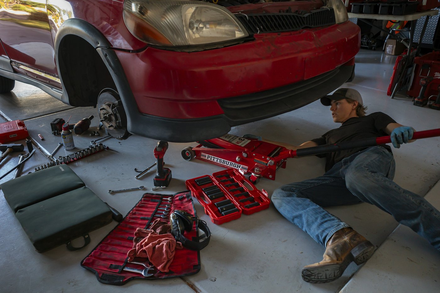 Mechanic working under a car with a jack and tools laid out