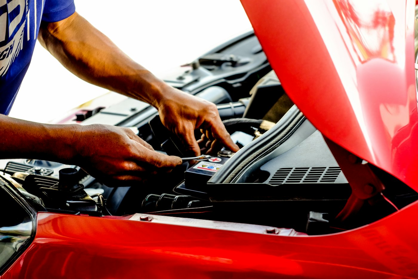 Mechanic working on a red car's engine outdoors